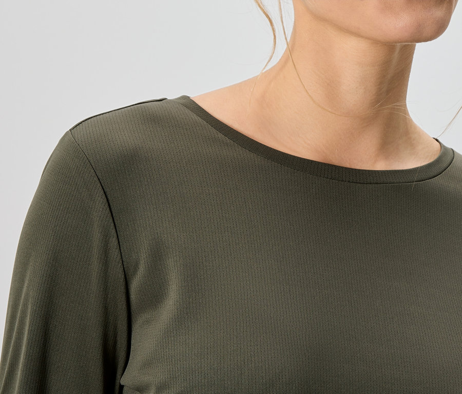 Nahaufnahme einer Frau, die ein olivgrünes, langärmeliges Oberteil trägt.