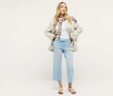 Eine Frau steht und trägt Angels Denim »Linn City« cropped, bleached blue, ein weißes T-Shirt, einen Blazer und einen Schal.