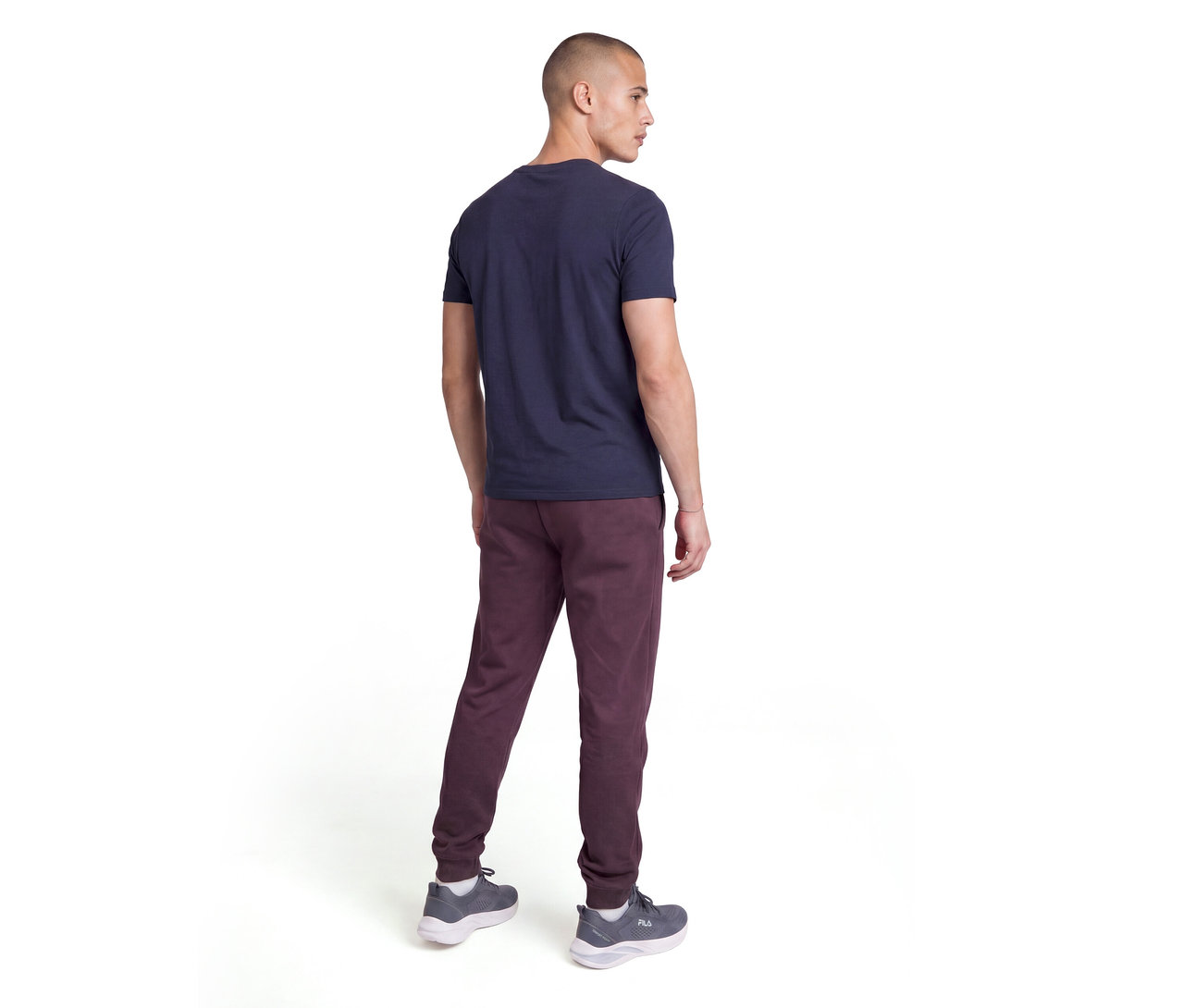 Ein Mann von hinten, trägt ein dunkelblaues T-Shirt, bordeauxrote Jogginghose und graue Turnschuhe. Er blickt über seine rechte Schulter.