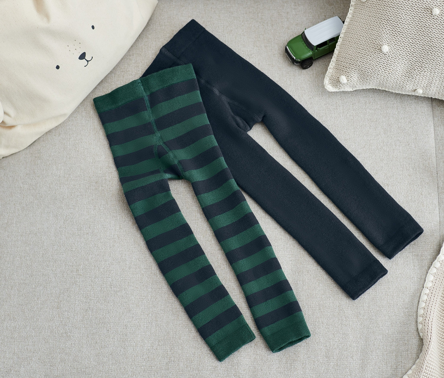 Zwei Paar Thermoleggings liegen auf einem beige Sofa, eines grün gestreift, das andere dunkelblau.