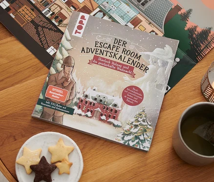 Auf einem Holztisch liegen das Escape-Adventskalenderbuch »Sherlock Holmes und die geisterhafte Weihnacht«, eine Kerze, eine Tasse Tee und ein Teller mit Keksen.