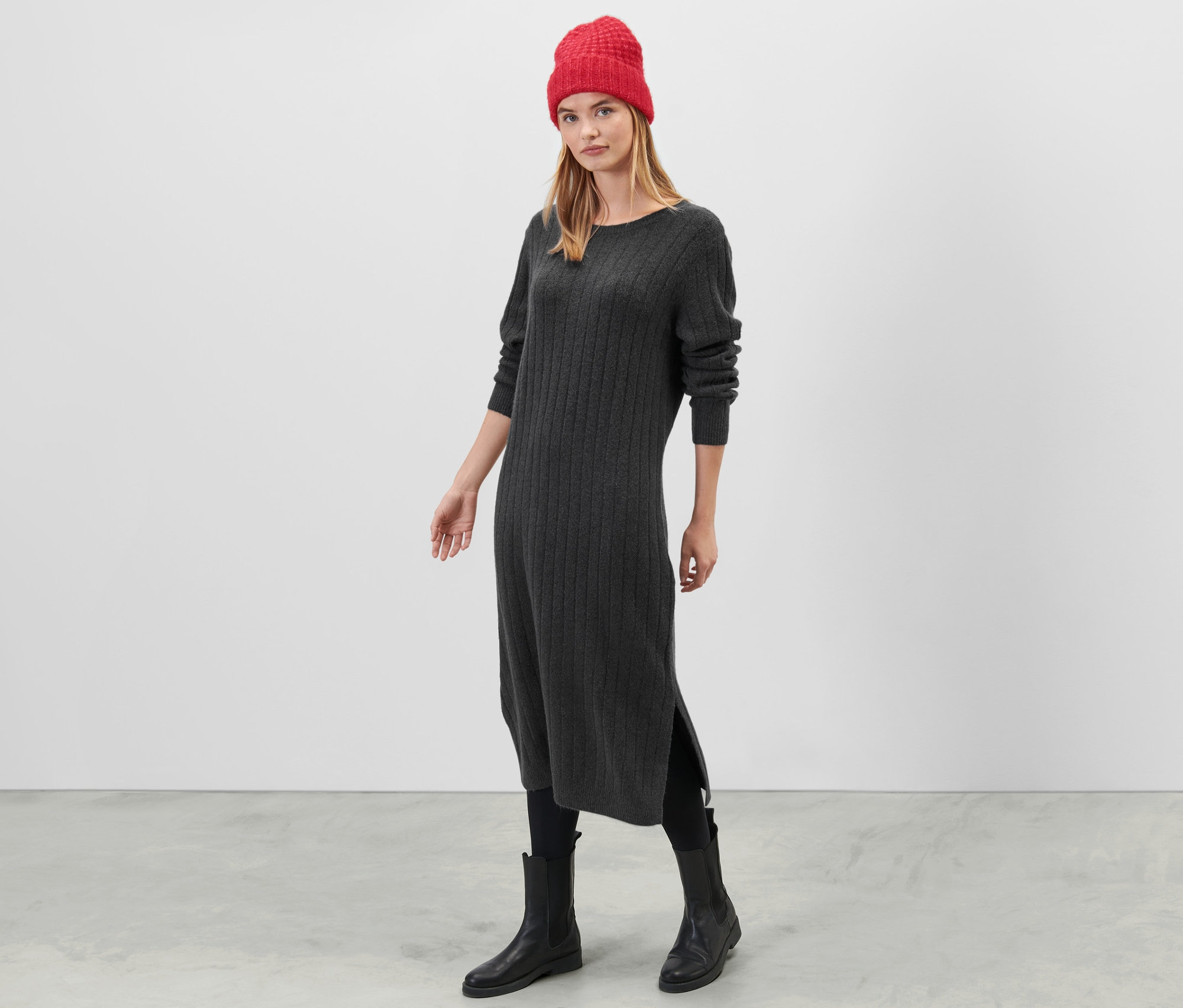 Frau steht und trägt ein graues, geripptes Strickkleid.