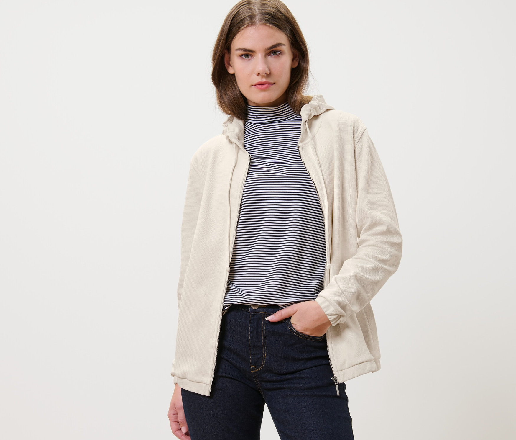 Frau trägt eine cremeweiße Sweatjacke und Jeans.