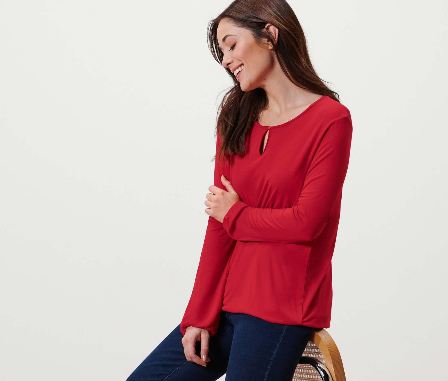 Frau sitzt auf einem Stuhl und trägt ein rotes Blusenshirt.