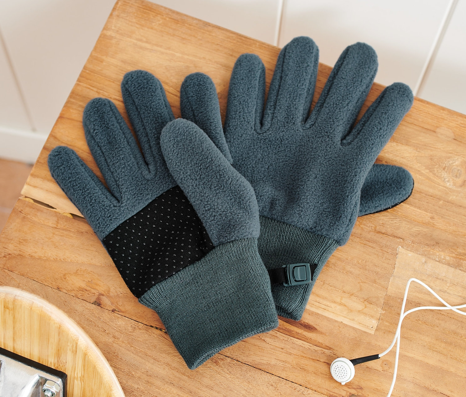 Zwei Kinder-Fleecehandschuhe liegen auf einer Holzbank neben einem Skateboard und Kopfhörern.