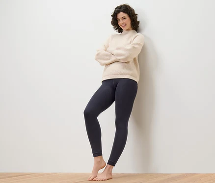 Frau steht mit verschränkten Armen an einer Wand und trägt eine gefütterte Leggings.