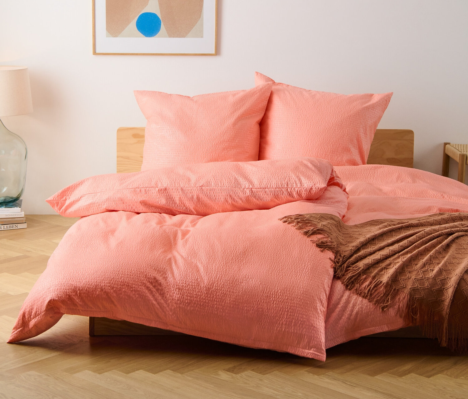 Eine Frontalaufnahme eines Bettes mit normalgroßer und übergroßer Seersucker-Bettwäsche in Pfirsichfarbe.