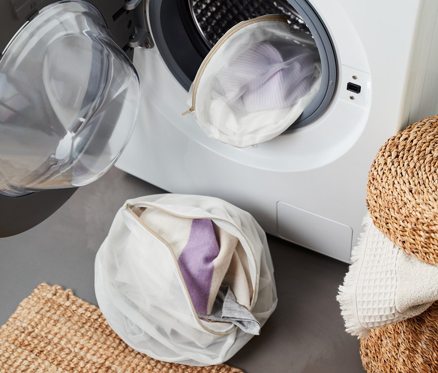 Zwei Wäschenetze, eines in der Waschmaschine, das andere auf dem Boden neben einer Matte.