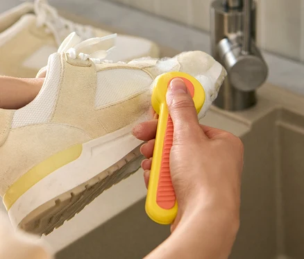 Frau putzt einen Schuh mit einer Schuhbürste über einem Waschbecken.
