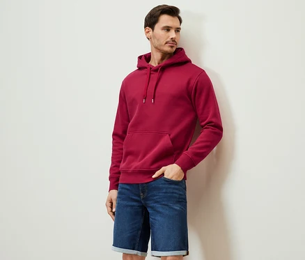 Mann posiert in rotem Hoodie und Jeansshorts.