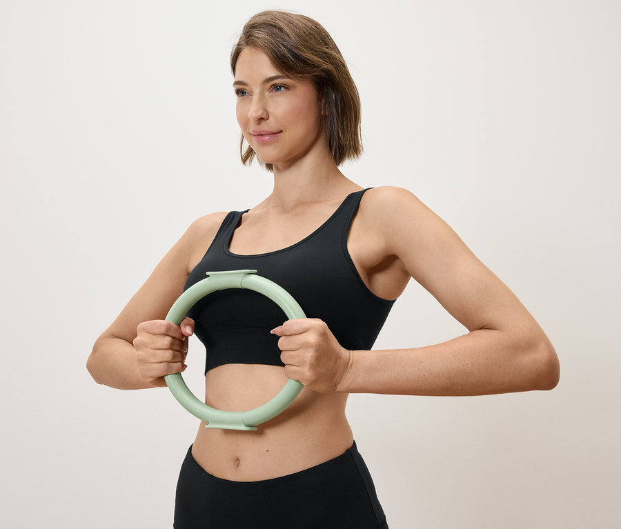 Frau hält einen hellgrünen Trainingsring vor sich, während sie ein schwarzes Sportoberteil und Leggings trägt.