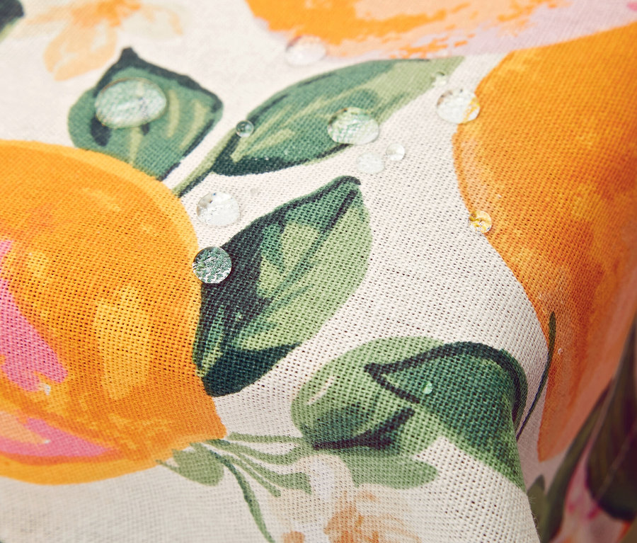 Detail einer abwischbaren Tischdecke mit Orangen- und Blumenmuster, auf der Wassertropfen liegen.