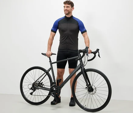 Mann steht neben einem Fahrrad und trägt ein blaues Fahrrad-Trikot.