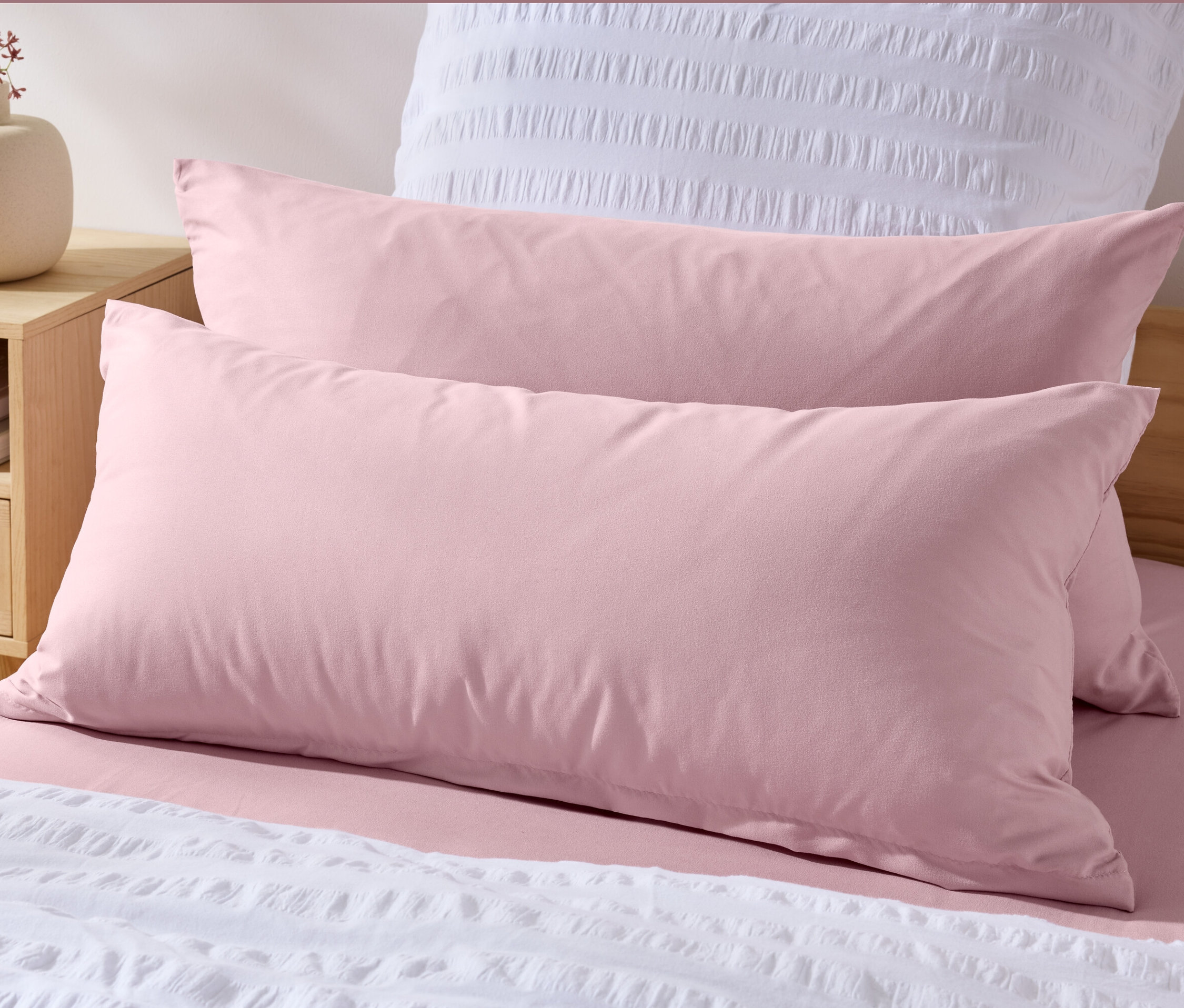 Zwei rosa Microfaser-Kopfkissenbezüge (ca. 80 x 40 cm) liegen auf einem Bett mit weißer Tagesdecke.