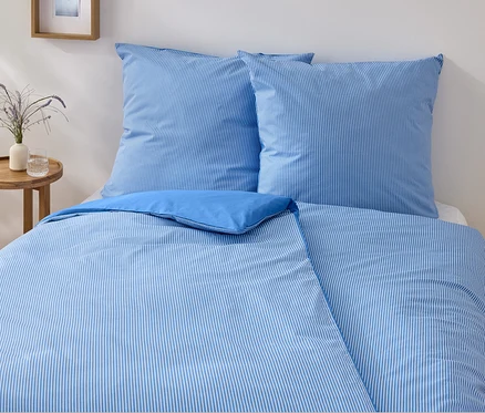 Ein blau-weiss gestreiftes Renforcé-Bettwäsche-Set in Normalgröße liegt auf einem Bett.