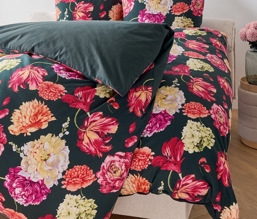 Blumige Bettwäsche auf einem Bett mit dunkelgrüner Decke.