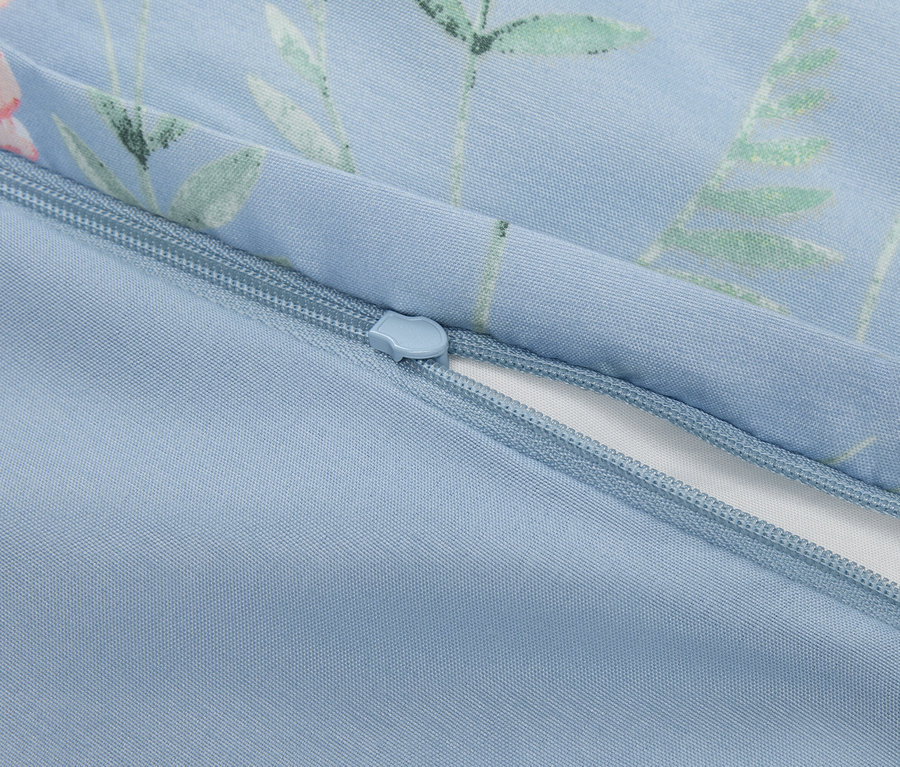 Detailansicht eines teilweise geöffneten Reißverschlusses auf einem hellblauen Kissenbezug mit Blumenmuster.