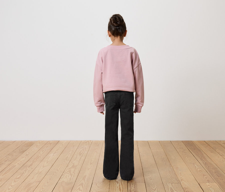 Mädchen mit dem Rücken zur Kamera trägt einen rosa Pullover und schwarze Jeans.