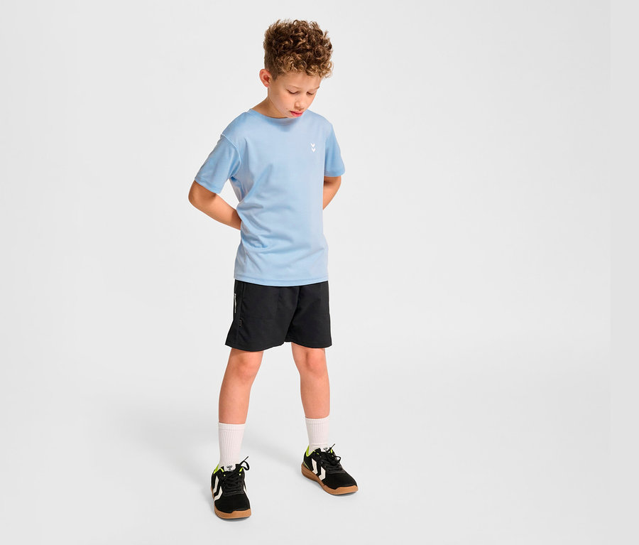 Junge posiert in hellblauem HUMMEL HMLJR pulse Trainings-T-Shirt und schwarzen Shorts.