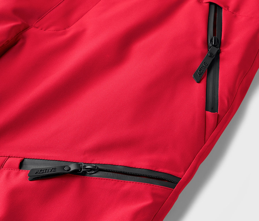 Detail einer roten Hose mit schwarzen Reißverschlüssen an den Taschen.