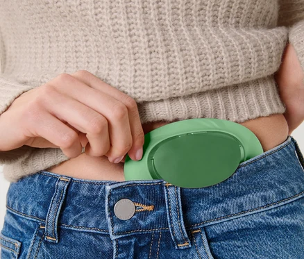 Frau steckt eine grüne Hülle in ihre Jeanshosentasche.