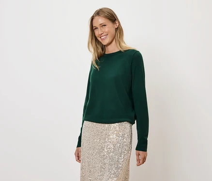 Frau mit blonden Haaren trägt einen grünen Pullover und einen goldenen Paillettenrock.