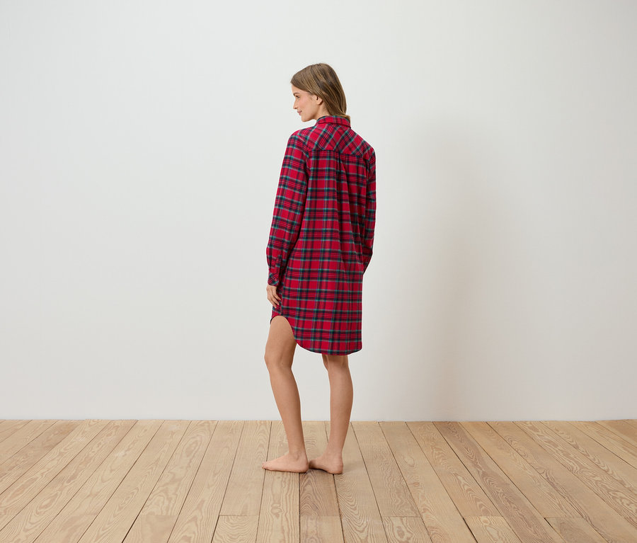 Eine Frau steht seitlich und trägt ein rot kariertes Flanellhemdkleid.