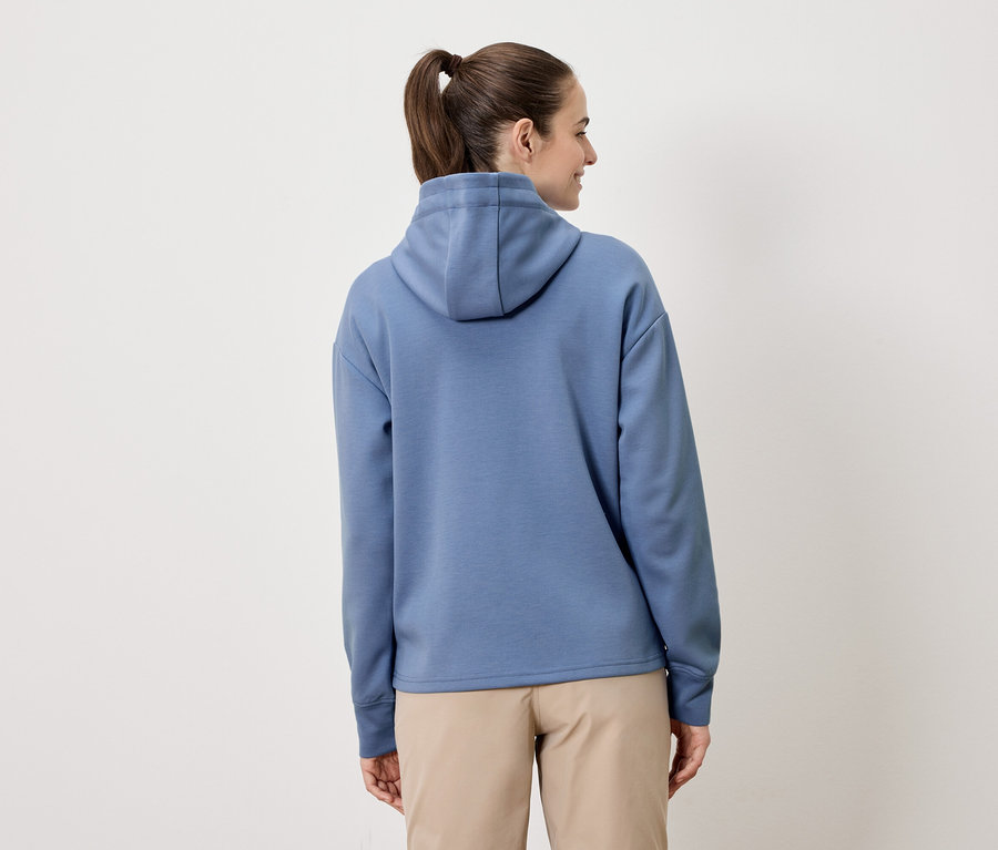 Eine Frau mit Pferdeschwanz trägt einen blauen Hoodie und beigefarbene Shorts.