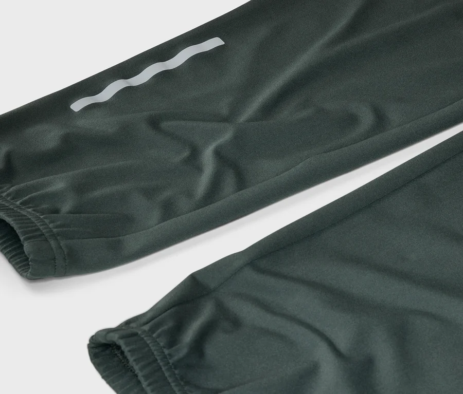 Nahaufnahme einer dunkelgrünen Hose mit elastischen Bündchen und einem reflektierenden, wellenförmigen Detail am Bein.