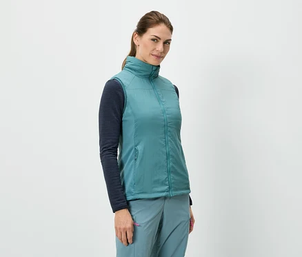 Eine Frau steht und trägt eine blaue Weste über einem langärmeligen Shirt, kombiniert mit blauen Hosen.