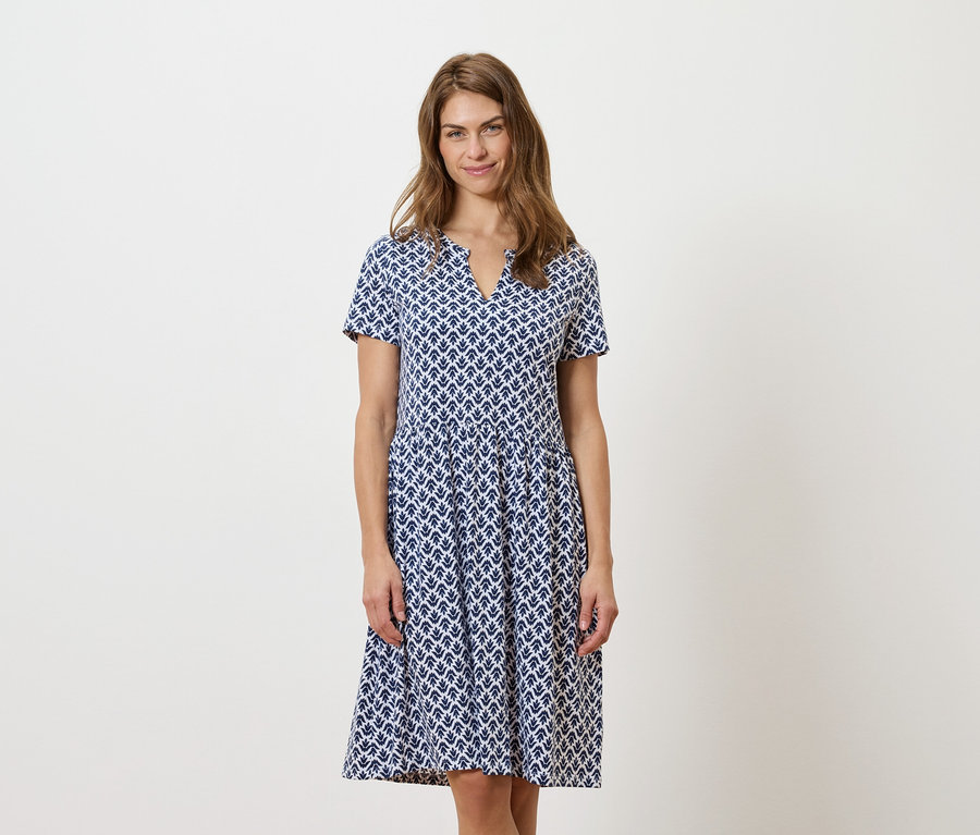 Frau steht und trägt ein blau-weißes Kleid.