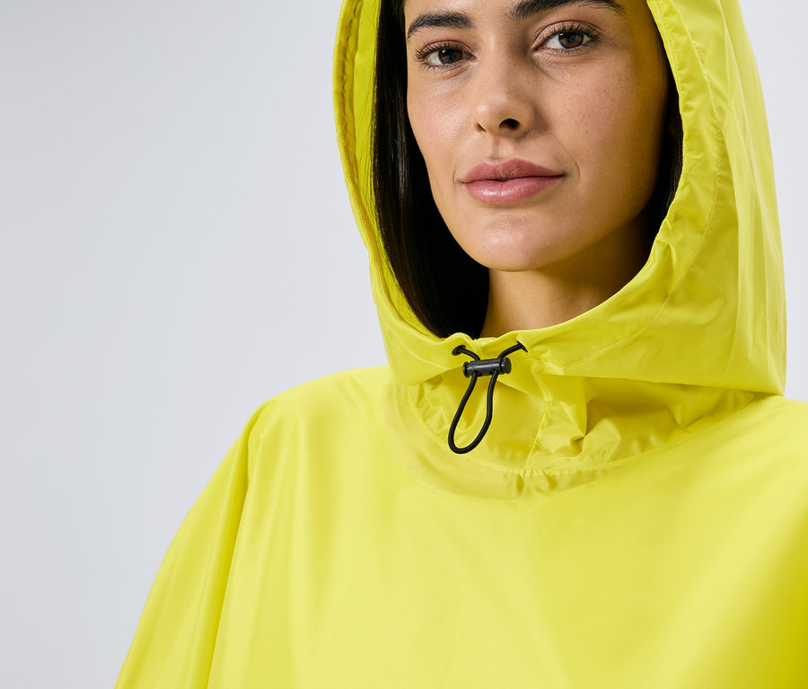 Frau mit Kapuze trägt einen gelben Regenponcho mit Kordelzug.