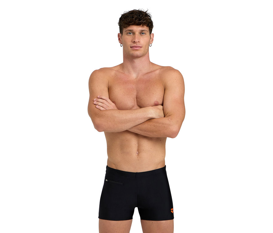 Mann mit verschränkten Armen, bekleidet mit schwarzen Badehosen.