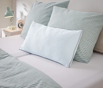 Nahaufnahme von Kissen und Bettwäsche mit Streifenmuster in Weiß und Grün auf einem Bett.