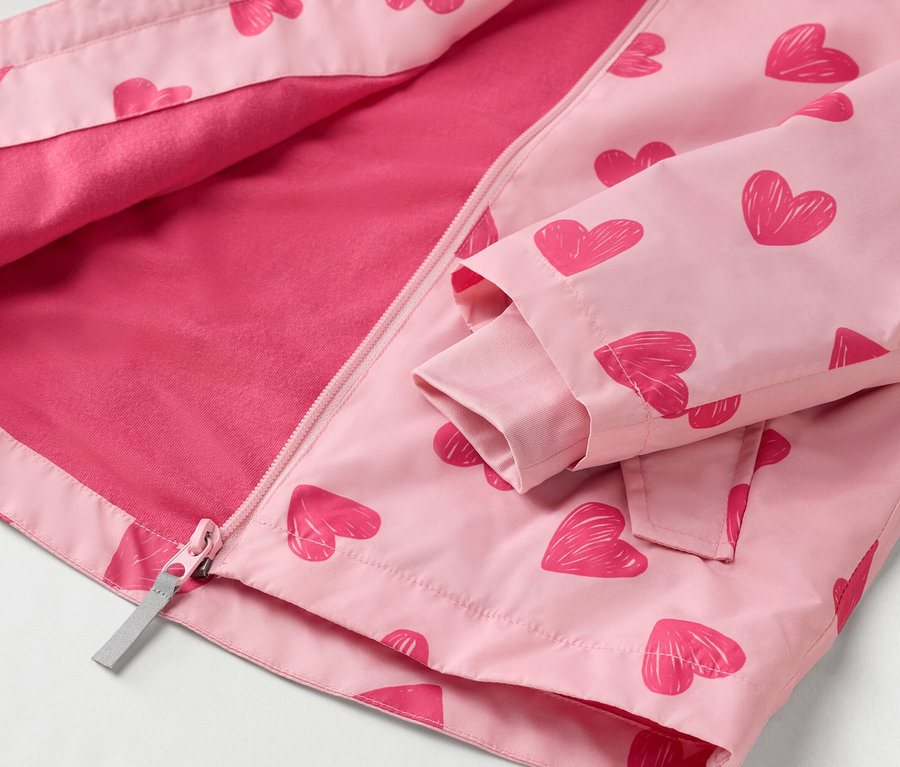 Nahaufnahme einer geöffneten, hellrosa Kinderjacke mit einem Muster aus roten Herzen und einem durchgehenden Reißverschluss.