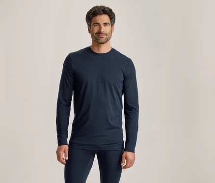Mann mit dunklem Haar und Bart, der ein dunkelblaues Langarmshirt und passende Hosen trägt, steht und blickt nach vorne.