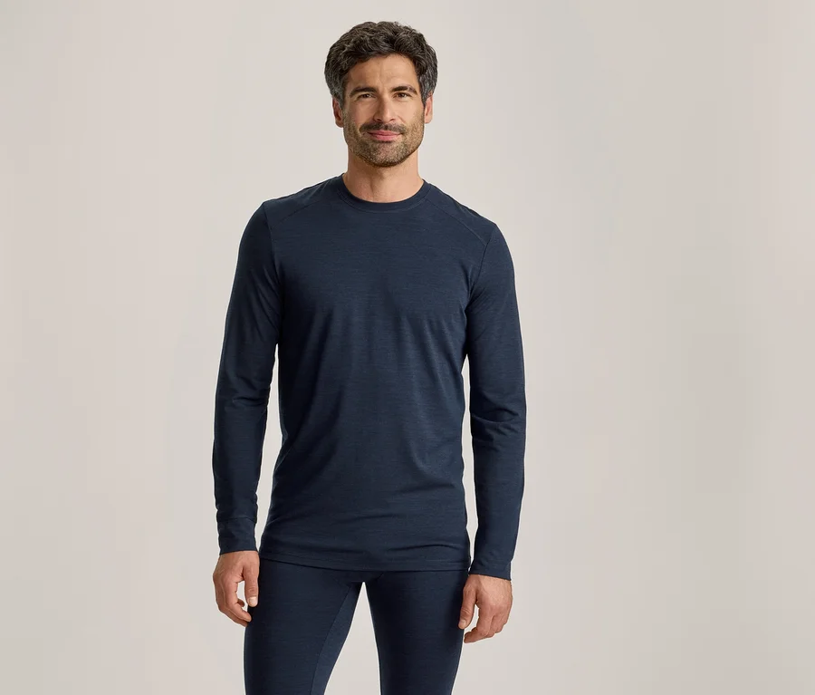 Mann mit dunklem Haar und Bart, der ein dunkelblaues Langarmshirt und passende Hosen trägt, steht und blickt nach vorne.