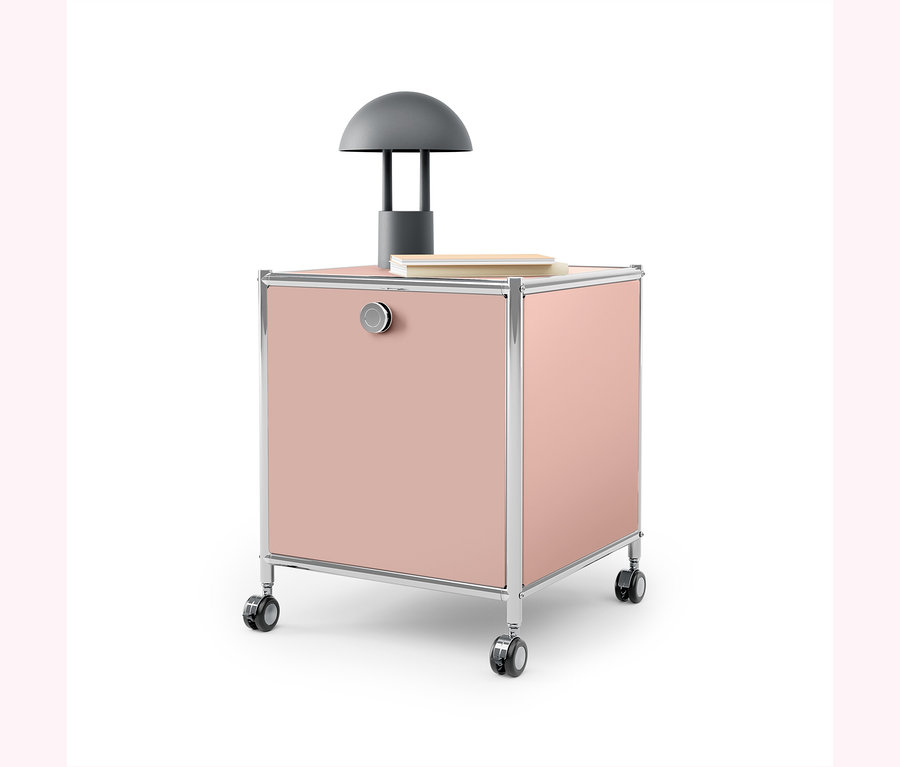 Rosa Rollcontainer mit Chromrahmen und grauer Lampe darauf.