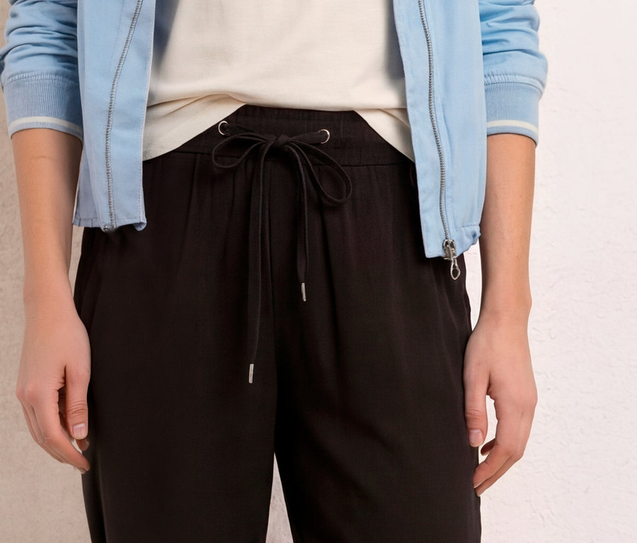 Eine Person trägt schwarze Street One 7/8-Culotte »EMMA« mit gebundenem Kordelzug, ein weißes Oberteil und eine hellblaue Jacke.