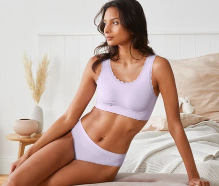 Frau sitzt auf einem Bett und trägt ein fliederfarbenes Seamless-Bustier.