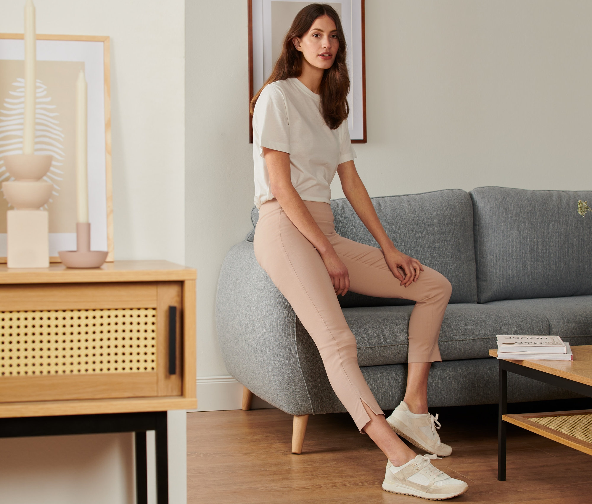 Frau sitzt auf einem grauen Sofa und trägt eine Stretchhose.