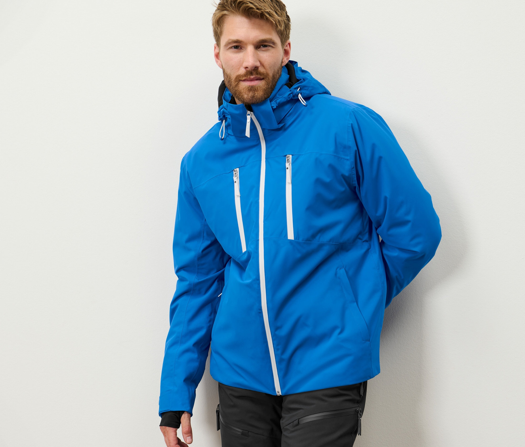 Mann mit Bart posiert in blauer High-Tech-Skijacke.