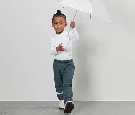 Ein Junge hält einen durchsichtigen Regenschirm und trägt eine Kleinkind-Regenhose.