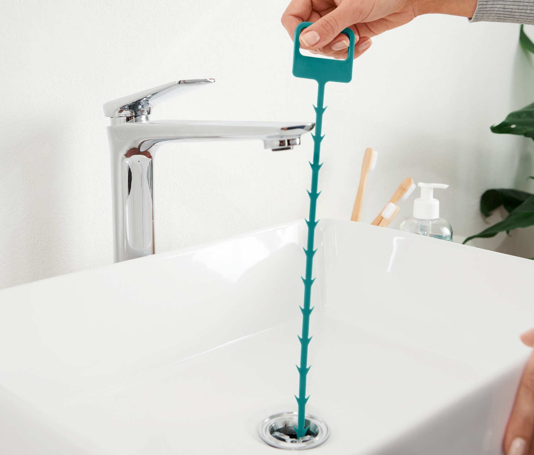 Eine Hand führt einen Abflussreiniger in den Abfluss eines Waschbeckens ein.