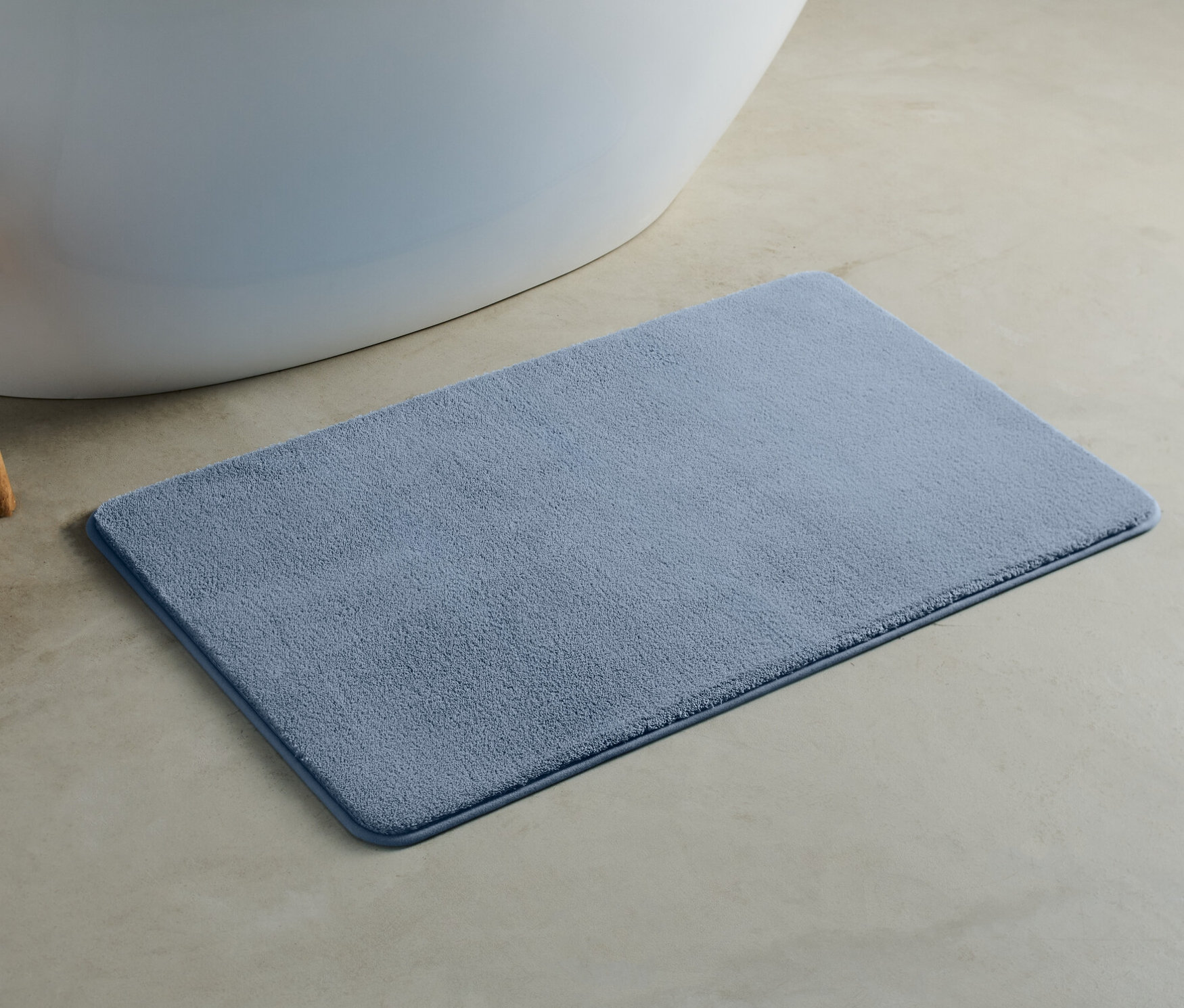 Eine blaue Badematte, ca. 100 x 60 cm, liegt auf dem Boden neben einer Badewanne.