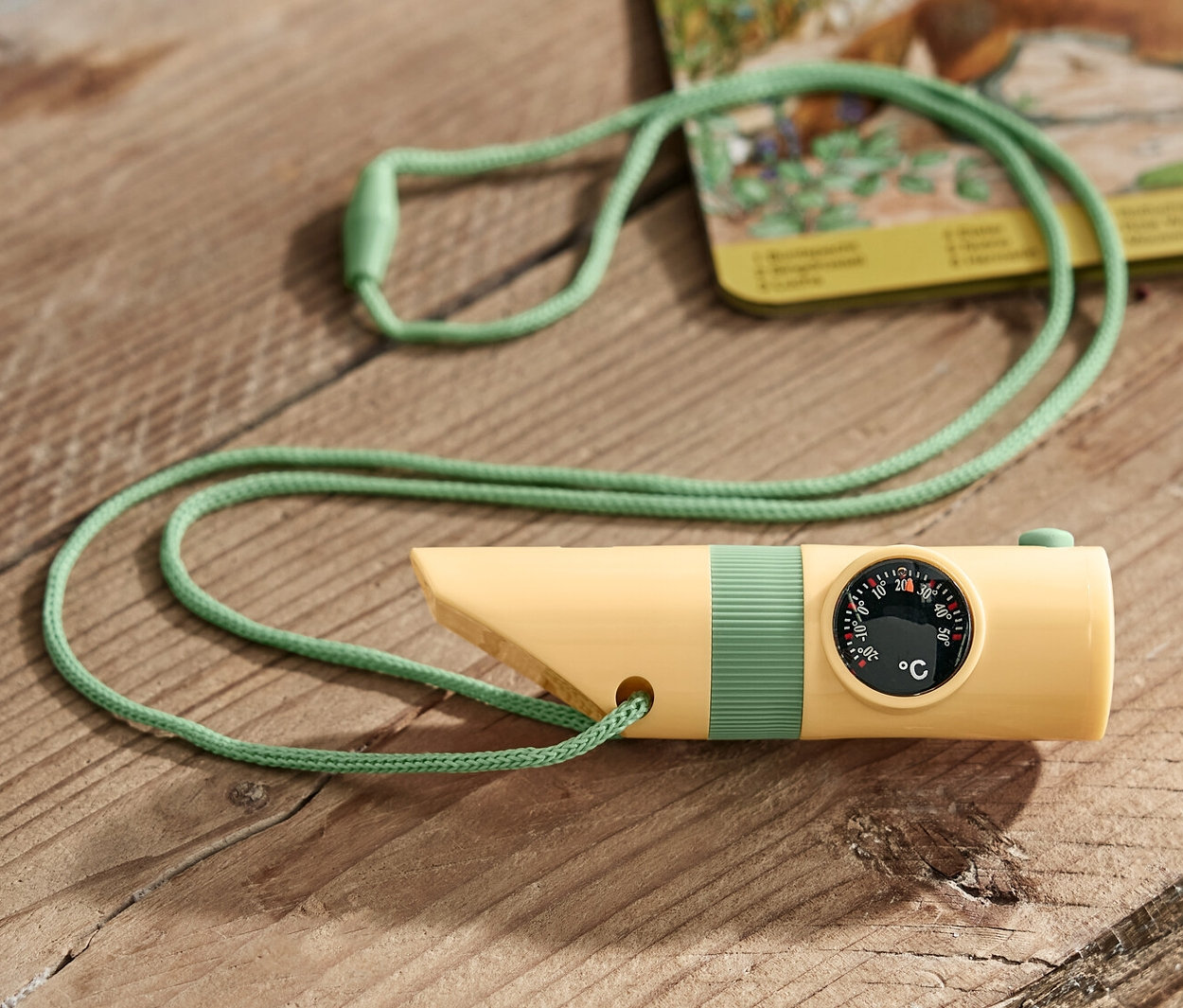 Gelbes kompaktes Outdoor-Tool mit grüner Schnur liegt auf einem Holztisch.