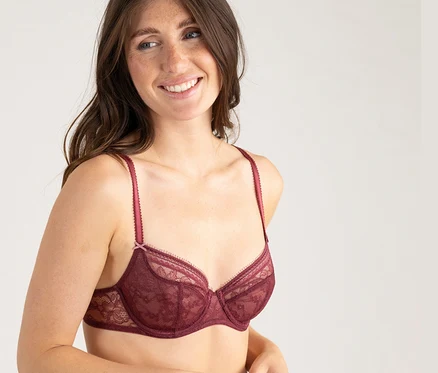 Lächelnde Frau mit langen Haaren trägt einen bordeauxroten Spitzen-Halbschalen-BH von Passionata »Jeanne«.