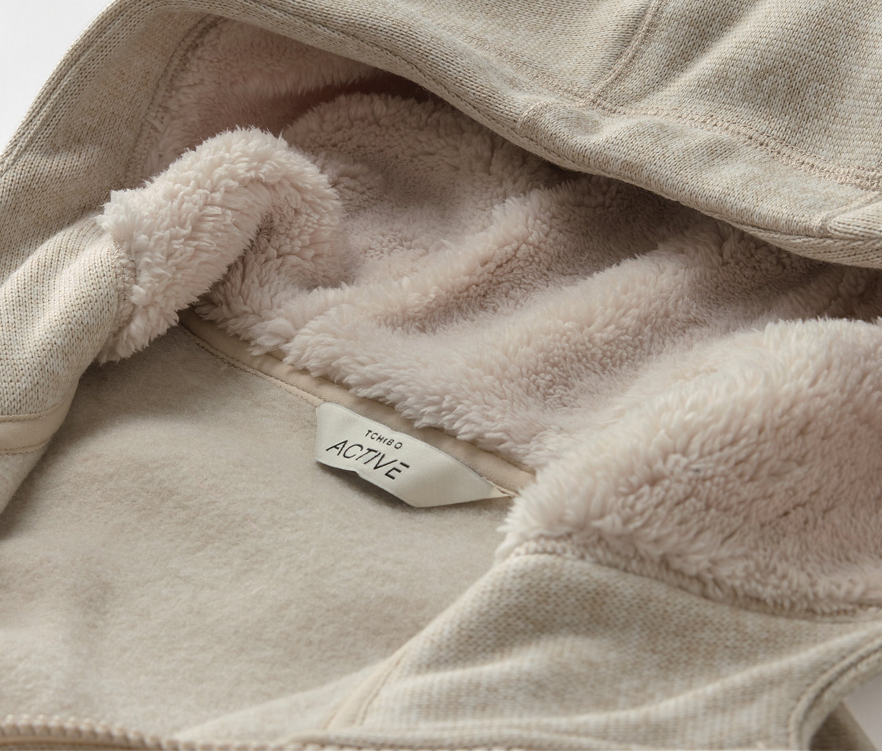 Detailaufnahme eines beigen Kapuzenpullovers mit Fleecefutter und ACTIVE-Etikett.