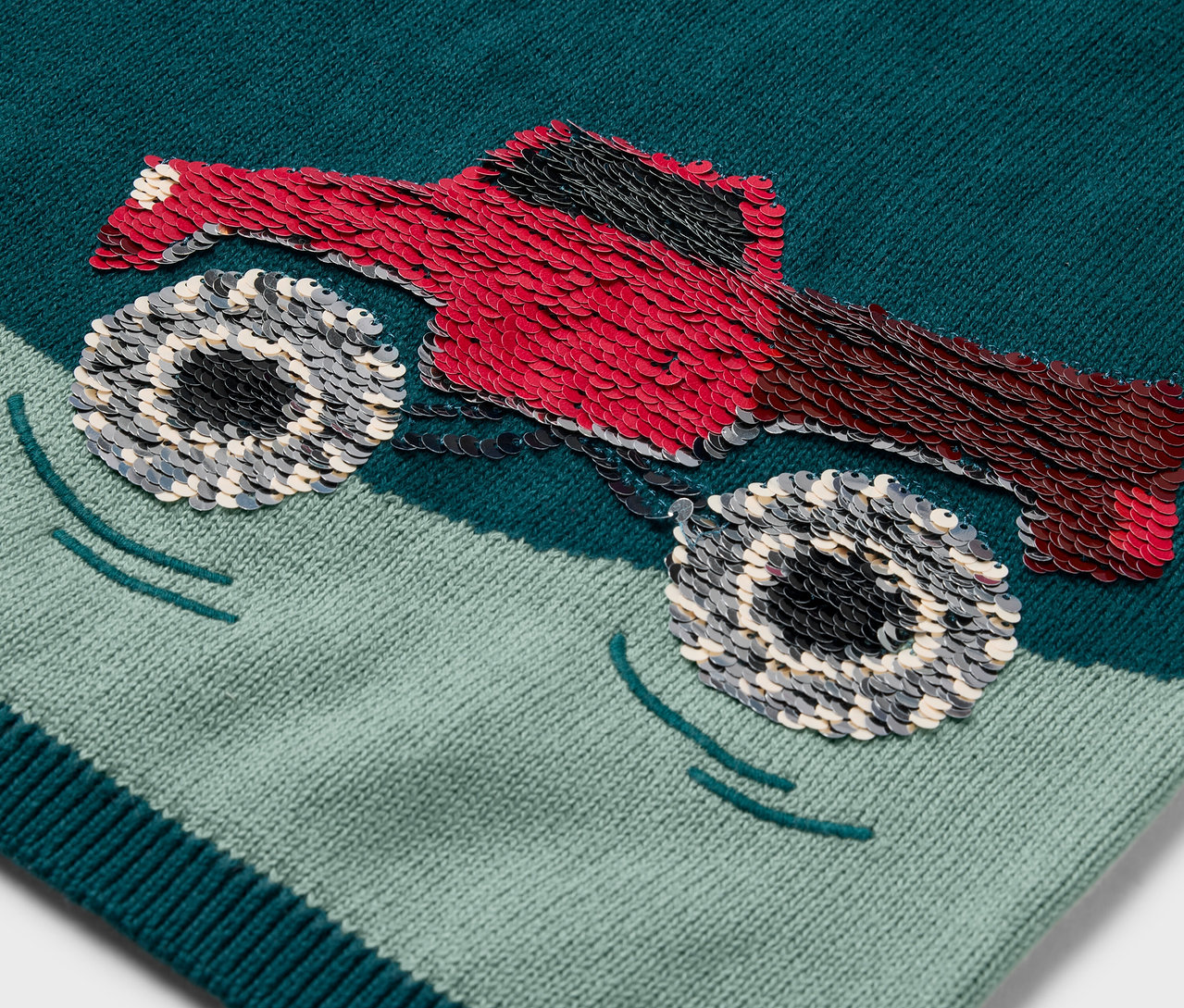 Detailaufnahme eines Kinder-Strickpullovers mit einem roten Monster-Truck-Aufnäher.