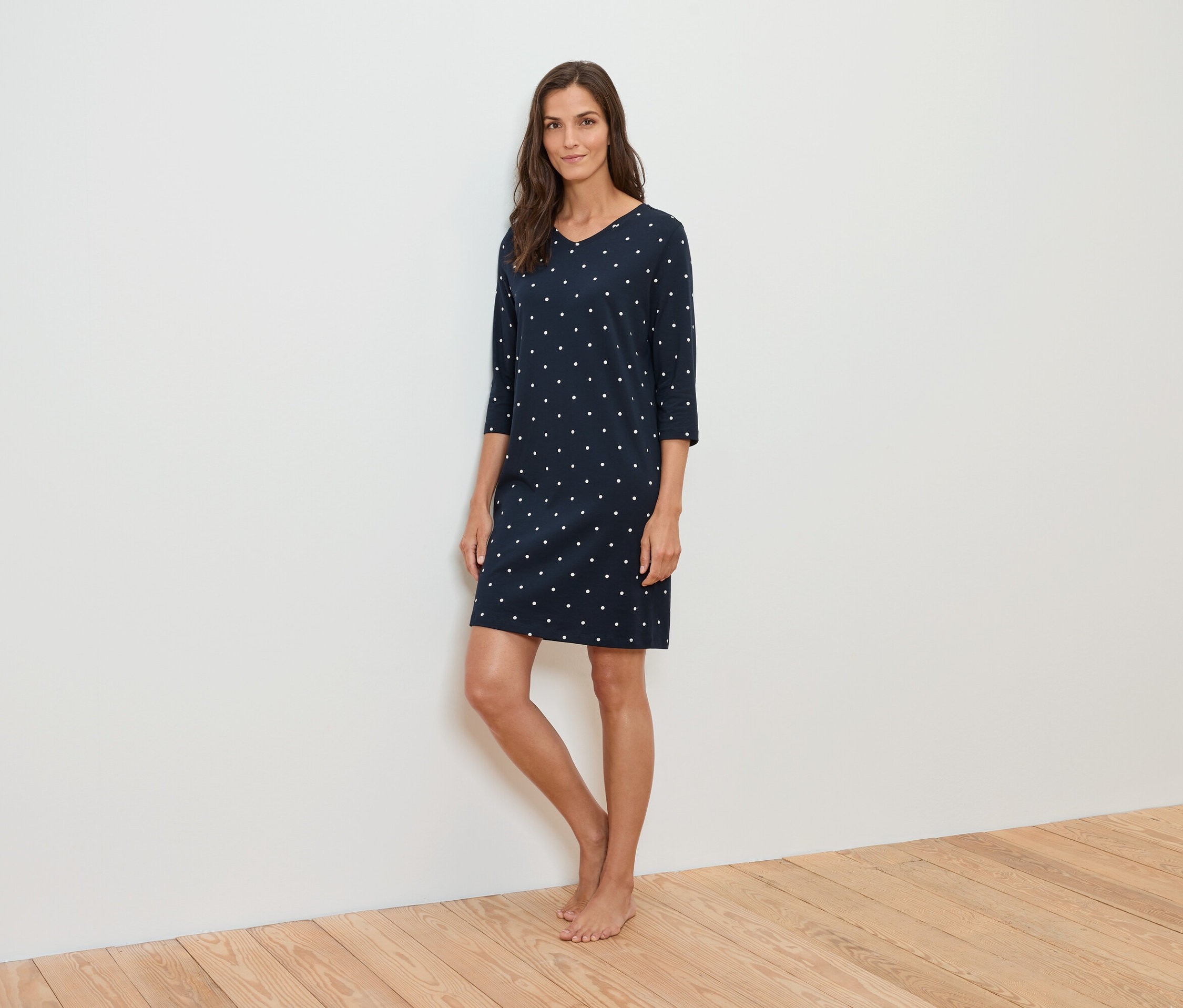 Eine Frau steht und trägt ein dunkelblaues Kleid mit weißen Punkten.